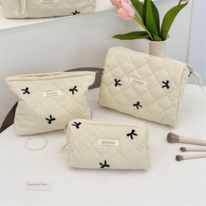 Three-piece set of cream quilted makeup bags with elegant black bow embroidery