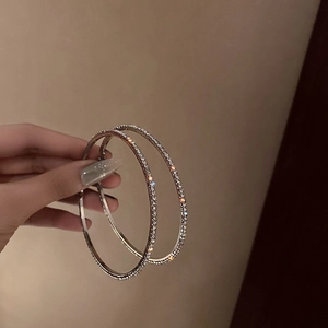 Macro detail of large silver hoop earrings with shimmering rhinestones held by hand