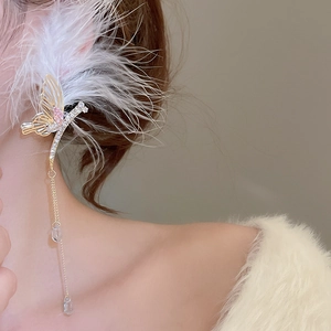 Macro shot of gold butterfly ear cuff with pink stones, white feathers, and long tassels