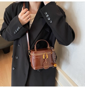 Detail of dark brown glossy box bag with dual zippers and leather hangtag shown on model