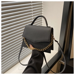 Detail of black crossbody bag with gold chain decoration and crocodile texture finish