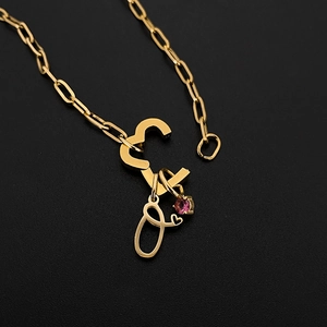 Detailed macro view of gold heart clasp with cursive initial O pendant and pink stone