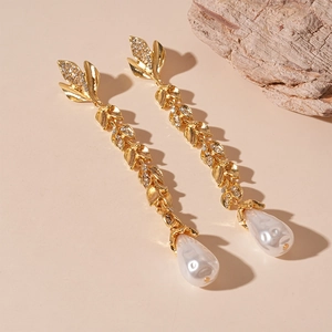 Elegant gold leaf tassel earrings with rhinestones and drop pearls on a textured rock