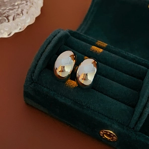 Macro detail of polished silver bean earrings resting on a green velvet jewelry box