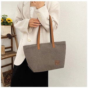 Detail of grey canvas tote bag with brown leather handles and square logo patch