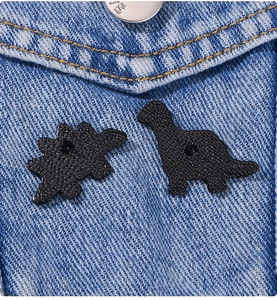 Dettaglio di due spille in smalto nero a forma di dinosauro su una giacca di jeans blu