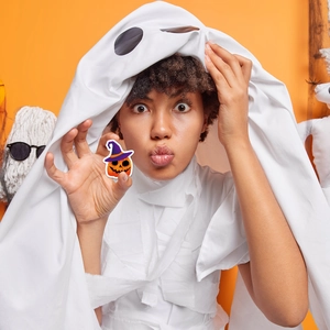 Kids Halloween pumpkin sticker with white ghost costume cape on vibrant orange background