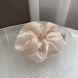 Macro view of champagne satin hair scrunchie with rhinestones on a glass tray