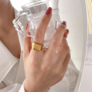 Golden wide band ring with embossed grid pattern shown in a lifestyle hand-held pose