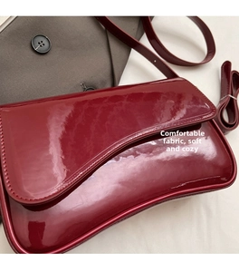 Detailed side view of dark red vintage glossy leather shoulder bag with curved flap