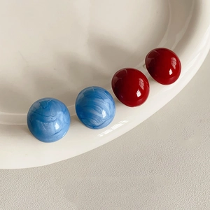 Nahaufnahme von minimalistischen Kugelohrsteckern in glänzendem Dunkelrot und marmoriertem Blau