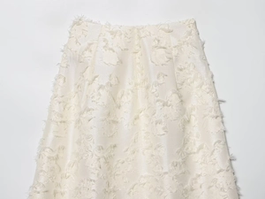 Detailopname van een parelwitte halflange rok met franjes jacquard stoftextuur