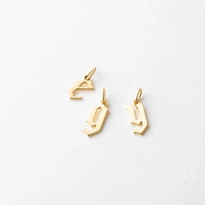 Detailed view of three polished gold Gothic letter pendants for custom jewelry