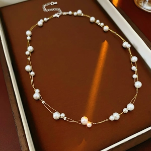 Détail macro du collier double couche avec perles blanches sur chaîne dorée fine
