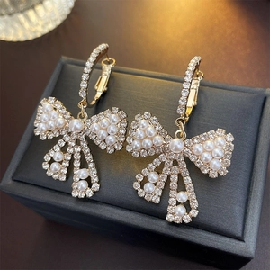 Eleganti orecchini a fiocco dorati con strass e perle su scatola portagioie nera