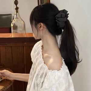 Elegant black bow hair scrunchie shown on a ponytail with a stylish fabric texture