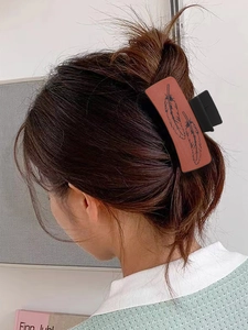 Detail of a brown textured leather hair claw clip with black feather patterns on hair