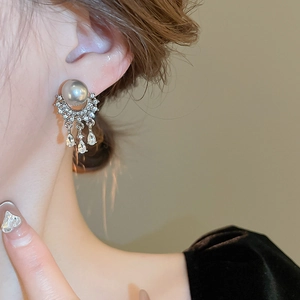 Close-up of dangling grey pearl earrings with sparkling zircon fringe on a model