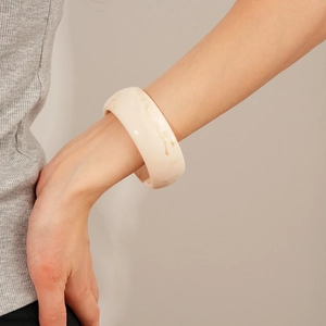Detail view of a thick cream resin bangle featuring a natural marble texture on a wrist