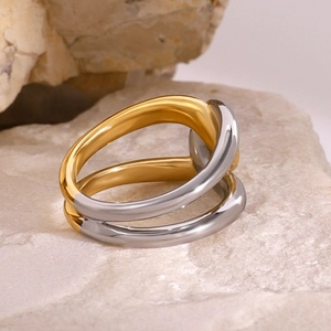 Polished gold and silver two-tone crisscross stainless steel ring on natural stone
