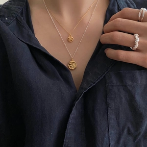 Close-up of layered gold necklaces with geometric pendants and silver twisted rope rings