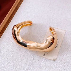 Detailed view of an irregular gold bangle with polished finish on white textured cloth