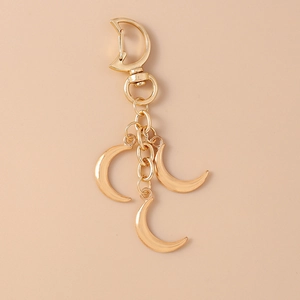 Close-up of golden moon keychain with star and moon charms on a beige background