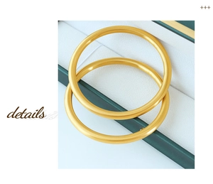 Detail of two matte gold minimalist solid round bangles placed on a dark green gift box