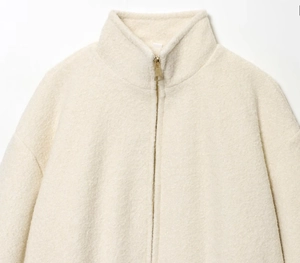 Detail of cream standing collar jacket featuring textured fleece and gold metal zipper