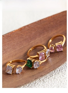 Detail of four gold-plated titanium steel rings with colorful zircon inlays on wood base