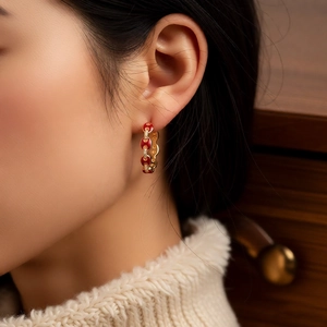Close-up of 18k gold-plated huggie earring with red enamel and zircon on a model