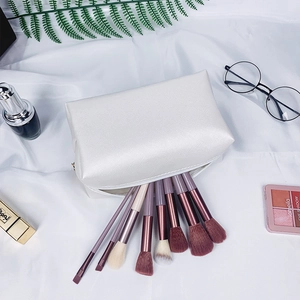 Flat lay of white faux leather makeup bag with pearl letter patch and brushes