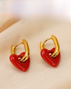 Detail of red enamel heart charms on gold U-shaped earrings over champagne silk fabric