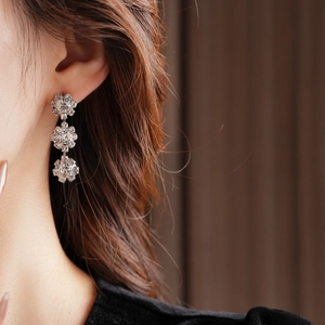 Close-up of silver rhinestone sunflower drop earrings worn on model's left ear