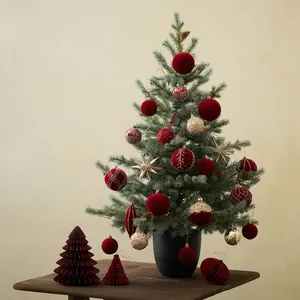 Mini PE Christmas tree in black pot with red and gold ornaments on a wooden desk