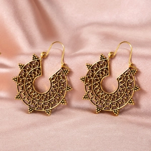 Detailed shot of vintage hollow-carved fan earrings on pink silk background
