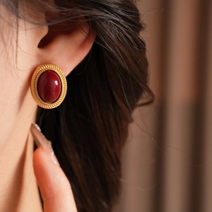 Close-up of vintage gold oval earrings featuring large red gemstones on ear