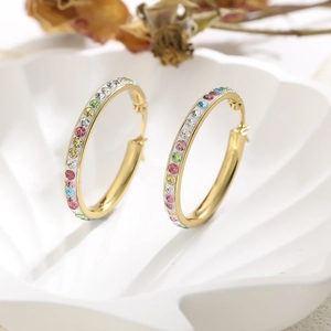 Detail of gold hoop earrings with colorful rhinestones and white enamel on a shell tray