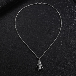 Detail of silver skeleton hand pendant with box chain on textured black background