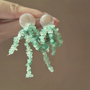 Détail de boucles d'oreilles fleuries avec coquilles blanches et pompons en pierres vertes
