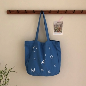 Detail einer blauen Canvas-Tragetasche mit weißem Buchstaben-Aufdruck an einem Wandhaken