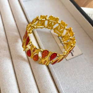 Close-up of golden vintage elastic bracelet with red and orange enamel teardrop charms