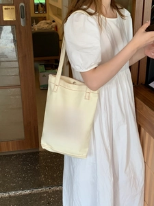 Close-up of cream canvas tote bag with brown HAPPY lettering and reinforced stitching
