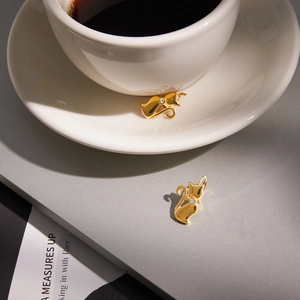 Golden stainless steel cat earrings with white zircon accents on a white coffee cup