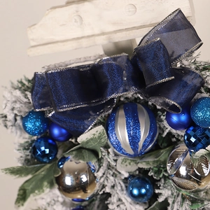 Detail of blue and silver Christmas ornaments with velvet bow and snow-dusted pine branches