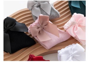 Detail showing various colors of girls' cotton socks with large bows and lace ruffles