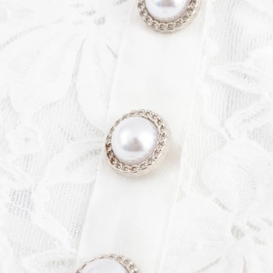 Détail d'une robe en dentelle blanche avec boutons de perles et bordure argentée