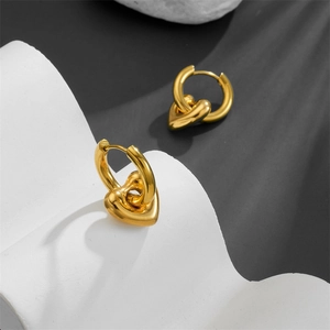 Close-up of golden puff heart earrings on white stone with artistic leaf shadows