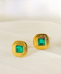 Close-up of square gold earrings with sunburst texture and emerald green zircon stones