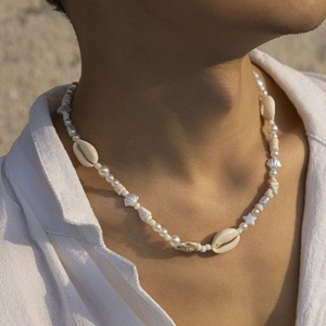 Close-up of a beach style shell and pearl necklace worn by a male model on white shirt